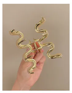Detailansicht einer stilvollen goldenen wellenförmigen Haarklammer mit beigen Details.