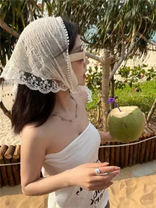 Primer plano de un pañuelo triangular vintage blanco de encaje y cuadros en playa.