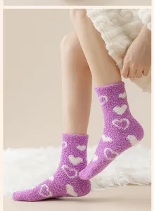 Detailansicht von lila Korallenfleece-Herzsocken auf weißem Kunstfellteppich für Winterwärme.