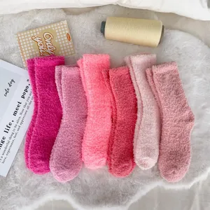 Close-up of fluffy coral fleece socks in six varied shades of pink laid on a white rug.