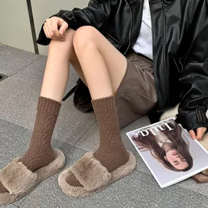 Detail shot of brown cable-knit mid-calf socks with fuzzy slippers and leather jacket