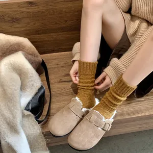 Close-up of mustard yellow thick knitted slouch socks styled with cozy shearling-lined clogs