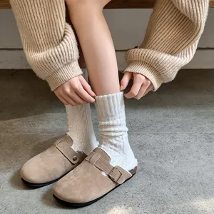 Detailed view of thick cream cable knit slouch socks paired with cozy fur-lined suede clogs