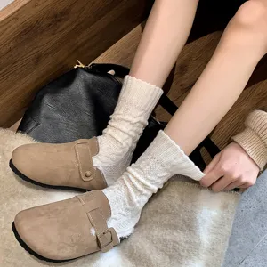 Close-up of cozy off-white cable knit slouch socks paired with beige suede clogs