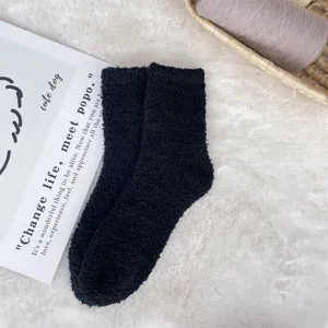 Close-up view of black fuzzy coral fleece socks with soft texture on a plush rug.