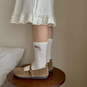 Close-up of white cable-knit socks with a small plaid bow detail on model's feet.