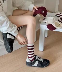 Lifestyle detail van bordeauxrode kuitkousen met witte strepen en elegante strikborduring