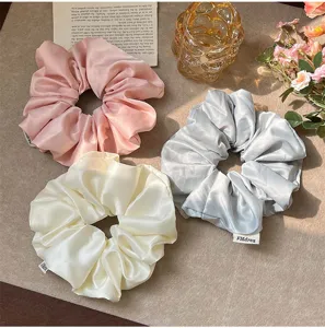 Detail view of oversized French vintage satin scrunchies in pink, cream, and silver-grey