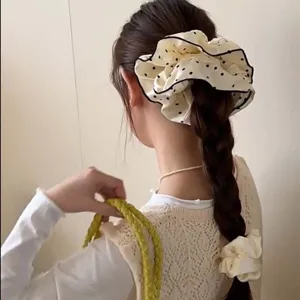 Detail view of an oversized cream polka dot lace scrunchie on a braided hairstyle.