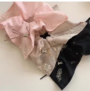 Close-up detail of pearl mesh scrunchies with rhinestone bows in pink, beige, and black
