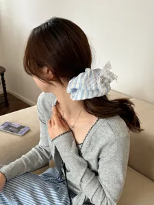 Detailansicht eines blau-weiß gestreiften Spitzen-Scrunchies an einem Pferdeschwanz.