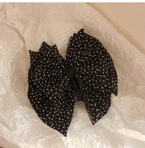 Gros plan d'une pince à cheveux à nœud noir à trois couches avec des pois blancs.