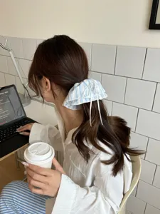 Blau-weiß gestreifter Spitzen-Haargummi mit Schleife, getragen von einem Model im Café-Stil.