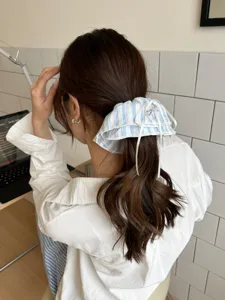 Detailansicht eines blau-weiß gestreiften Spitzen-Haargummis mit weißer Schleife im Haar.