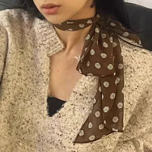 Primer plano de un pañuelo de seda marrón con lunares anudado con elegancia al cuello