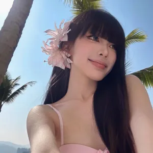 Primer plano de una pinza para el pelo con lirio rosa sobre cabello oscuro y fondo tropical
