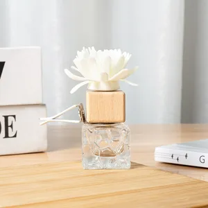 Close-up of car vent diffuser bottle with wooden cap, white flower and metal clip on board.
