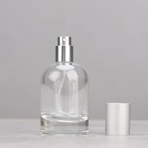 Clear glass perfume spray bottle detail showing the pump mechanism and separate silver cap.