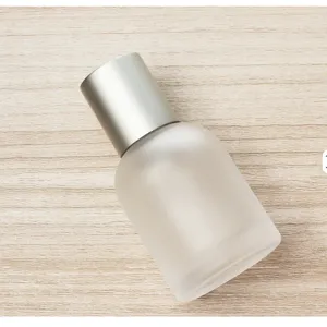 Frosted glass cosmetic spray bottle detail, silver metallic cap, minimalist empty container.