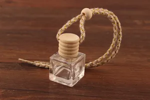 Close-up detail of a clear square glass perfume bottle with wooden cap and hanging rope.