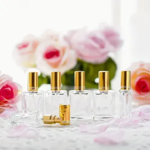 Clear glass refillable perfume atomizers with shiny gold caps and sprayers, elegant floral detail.