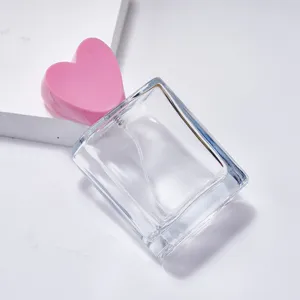 Detailaufnahme einer klaren quadratischen Parfümflasche mit rosafarbenem Herzdeckel und Spray.
