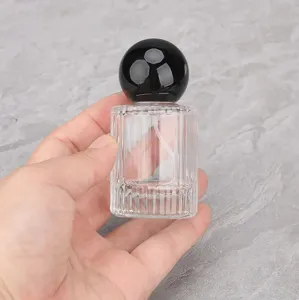 Clear glass perfume bottle detail shot featuring a round black cap and portable spray nozzle.