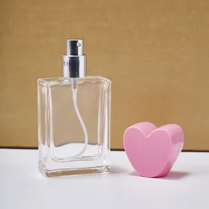 Klares Glas-Parfümfläschchen im Detail mit rosa Herzverschluss und Silberzerstäuber.