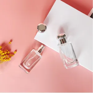 Detailed shot of clear glass refillable perfume atomizers on pink surface with dried flowers.