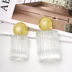 Transparant glazen parfumflesje met gouden bolvormige dop, lege cosmetische monsterhouder.