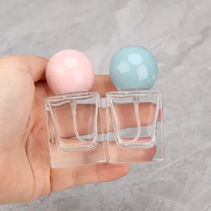 Clear square glass perfume atomizers with pink and blue ball caps for travel use.