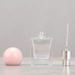 Close-up detail view of a clear glass perfume bottle with a pink round cap and spray pump.