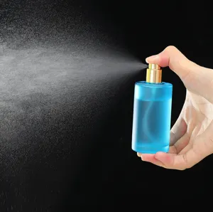 Primer plano detallado de un frasco atomizador de perfume de vidrio esmerilado azul en mano.