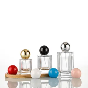 Detail view of square glass perfume bottles with round caps on wooden tray with colorful balls.