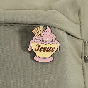 Primer plano de un pin de esmalte de cupcake rosa con texto religioso sobre tela verde