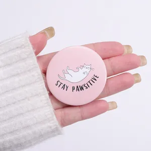 Close-up of a cute pink cat tinplate badge with Stay Pawsitive slogan on a hand