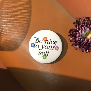 Round tinplate badge with 'be nice to yourself' quote on brown leather background