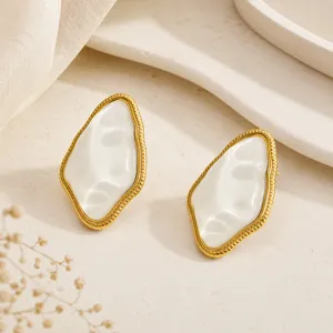 Close-up of irregular geometric gold-plated earrings with white resin inlay texture.
