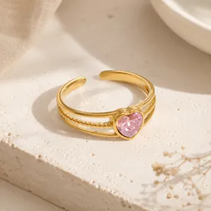 Primo piano di un anello in acciaio dorato con cuore in zircone rosa su pietra