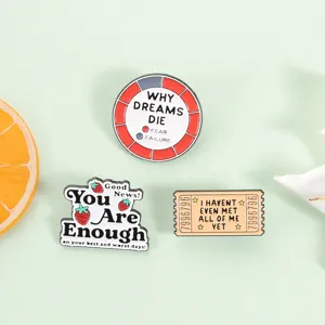 Makroansicht von drei kreativen Emaille-Pins mit Motivationssprüchen auf grünem Grund.
