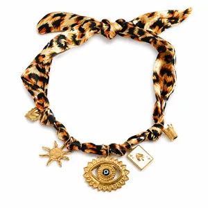 Macro detail of leopard print silk scarf necklace with evil eye and gold charms