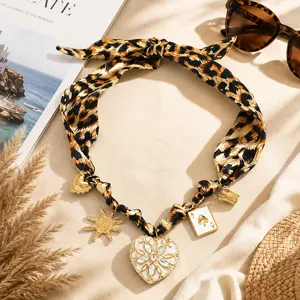 Detailed view of leopard print silk scarf necklace with gold heart and sun charms.