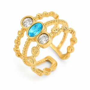 Primo piano di un anello a tre strati in acciaio dorato con zirconi blu e trasparenti.