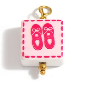 Detail view of square glass charm featuring pink ballet flat shoes with gold-toned loop