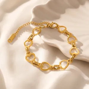 Gros plan d'un bracelet à maillons cœur en acier titane doré sur une coque blanche.