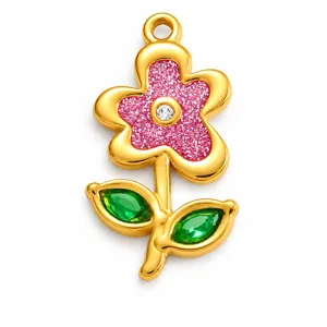 Detailed macro shot of a gold-plated flower pendant with pink glitter and green gems.