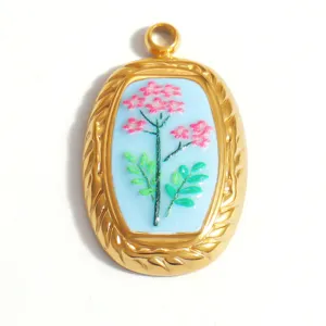 Oval stainless steel pendant with pink floral enamel design and twisted gold frame detail.