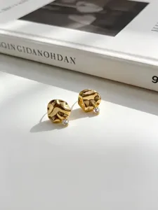 Vista detallada de pendientes dorados texturizados con circón sobre un libro blanco