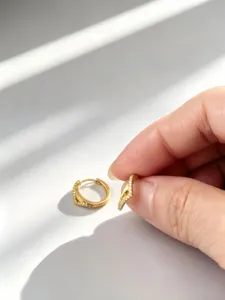 Detailopname van een hand die een V-vormige gouden oorring met zirkonia pavé vasthoudt
