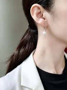Dettaglio di orecchino a cerchio in argento con perla bianca pendente su modella